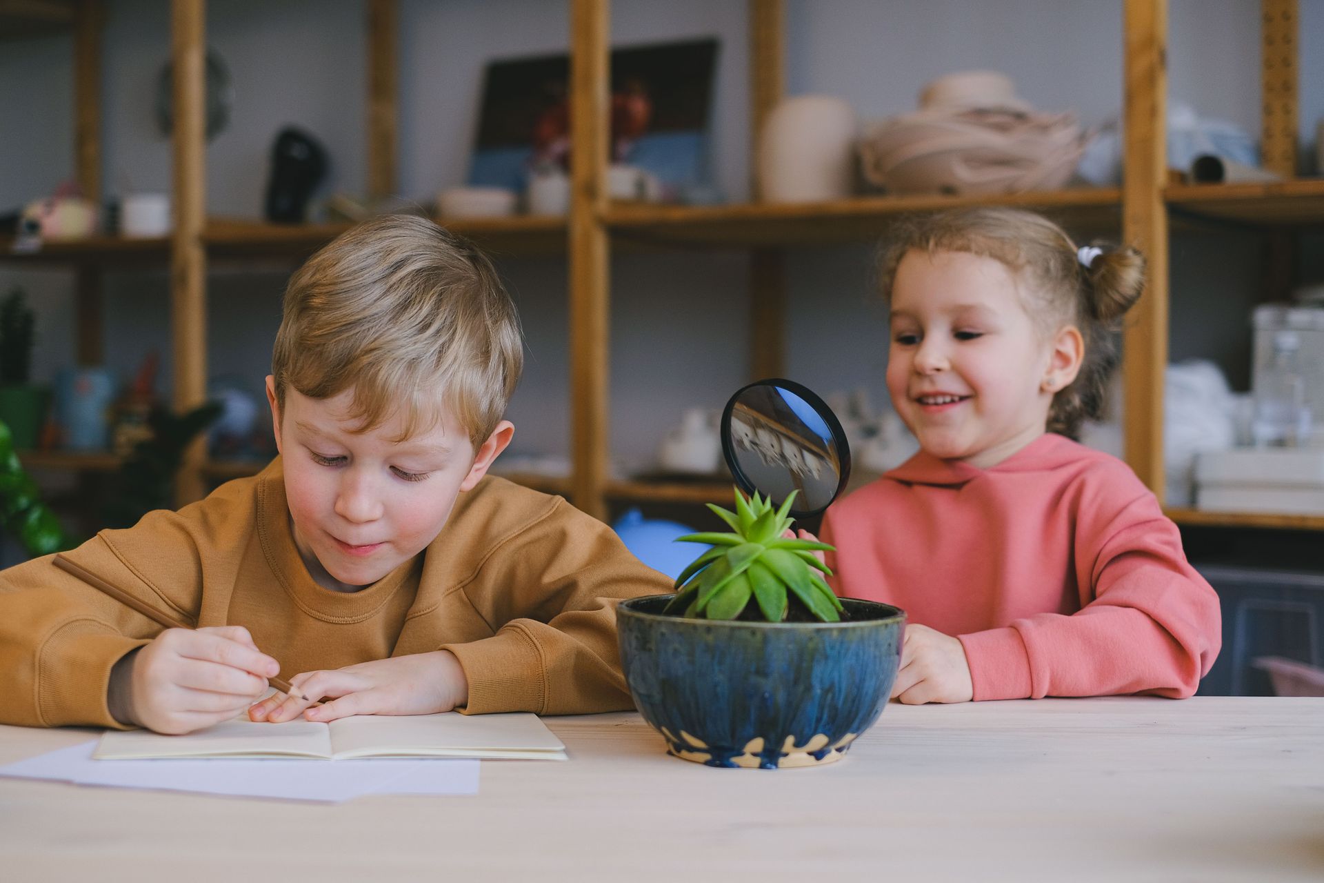 Two kids engaging in creative study with plants and magnifying glass indoors.